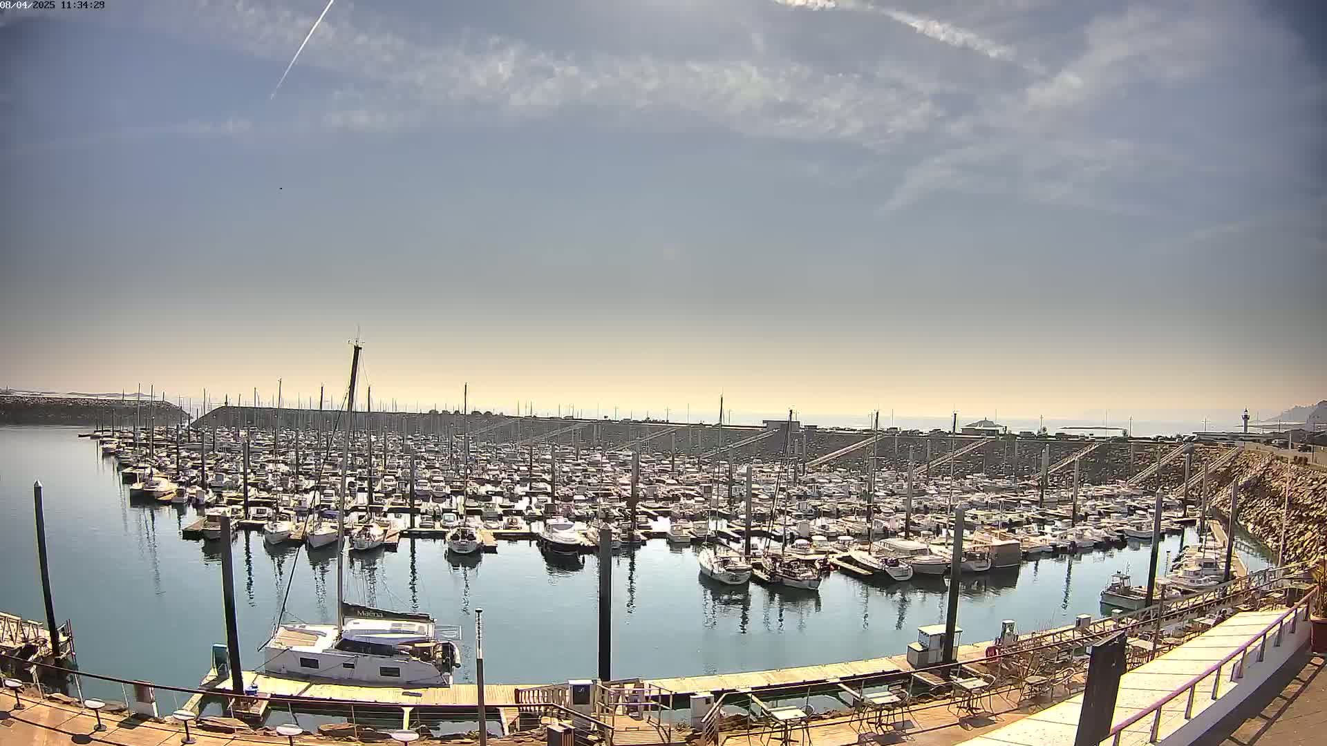 A large marina filled with numerous boats is seen under a mostly sunny sky with a few scattered clouds.