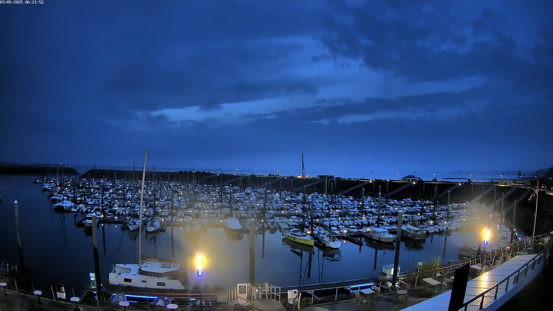 A large marina filled with numerous boats is visible at twilight under a mostly cloudy sky.