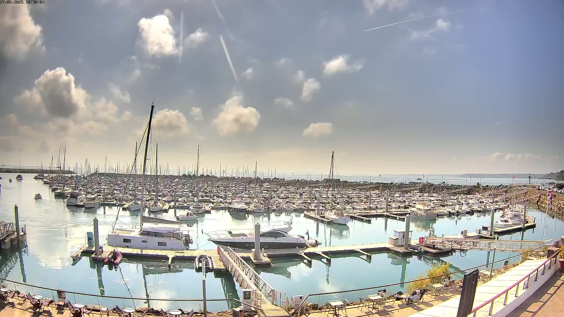 A large marina filled with numerous boats and yachts is seen under a partly cloudy sky.