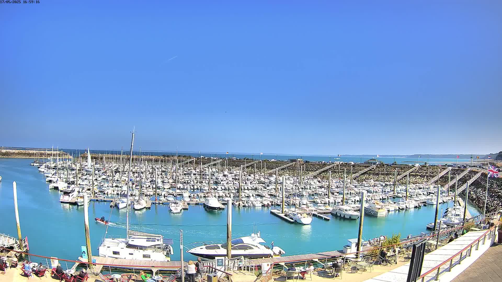 A large marina filled with numerous boats is situated on calm, teal water under a clear blue sky.
