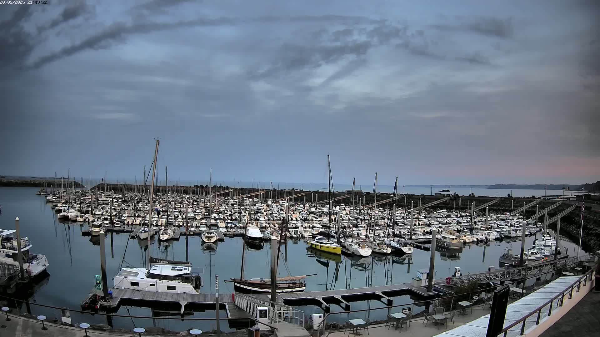 A large marina filled with numerous sailboats and motorboats is shown under a mostly cloudy sky.