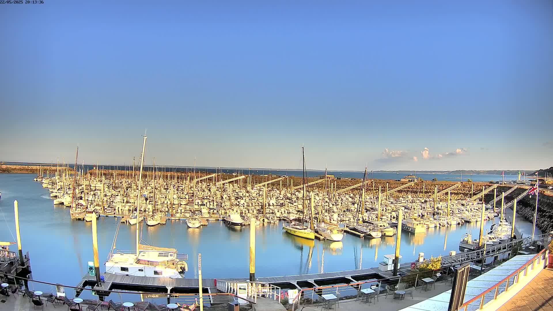 A calm harbor filled with numerous sailboats and motorboats under a clear blue sky.