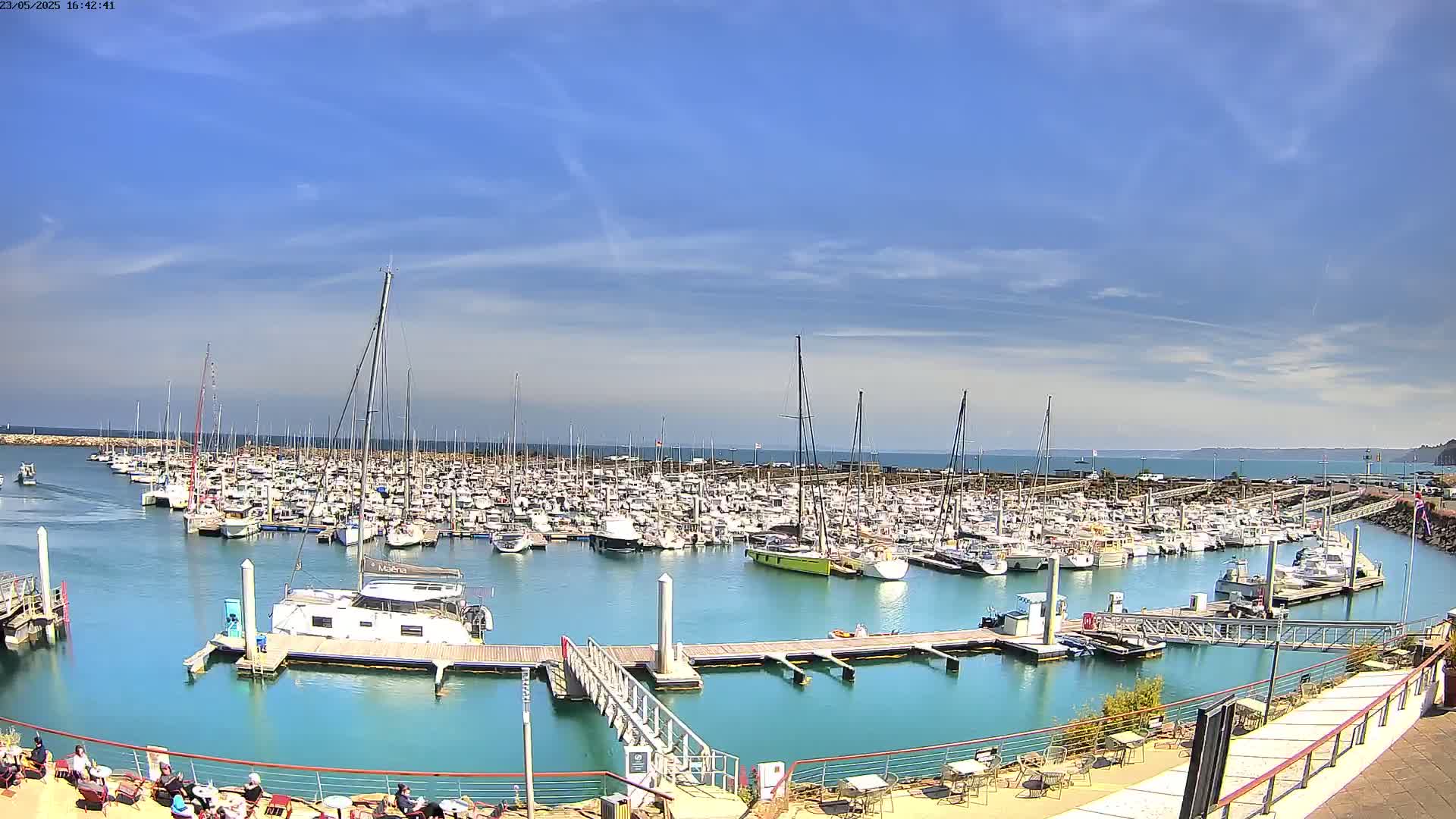 A large marina filled with numerous boats and yachts is shown under a mostly sunny sky with a few scattered clouds.