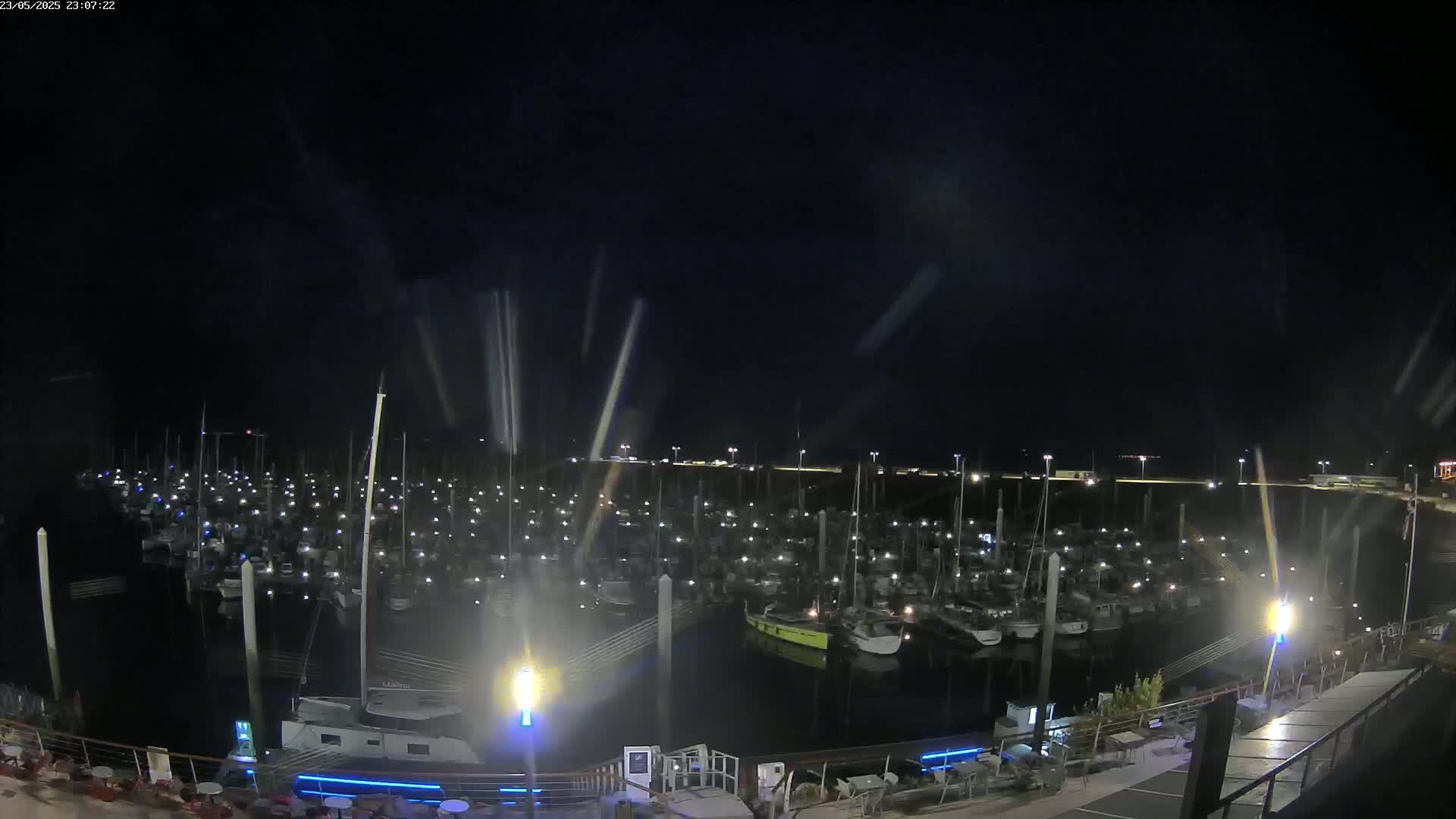 A nighttime view of a marina filled with numerous boats, illuminated by their lights under a dark, possibly rainy sky.