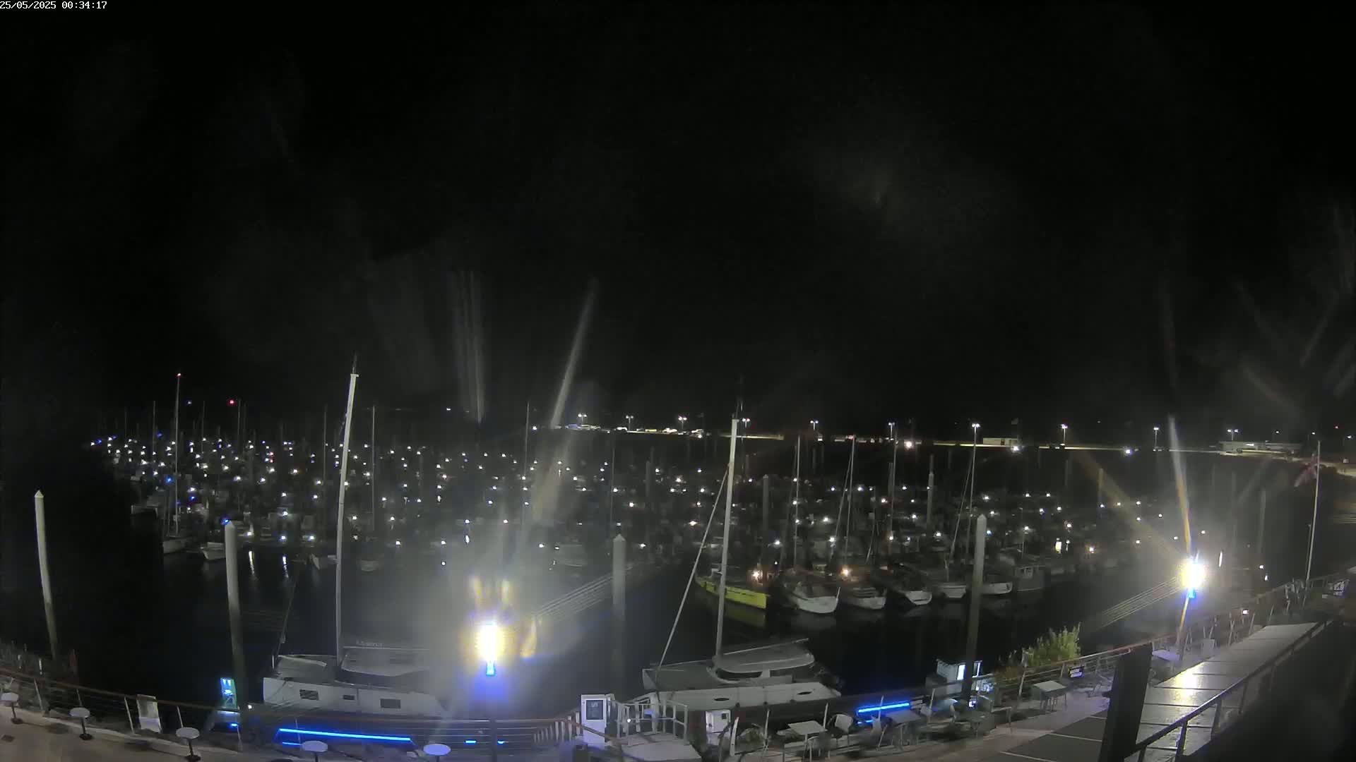 A nighttime view of a marina filled with numerous boats, illuminated by lights, under a dark, possibly overcast sky.