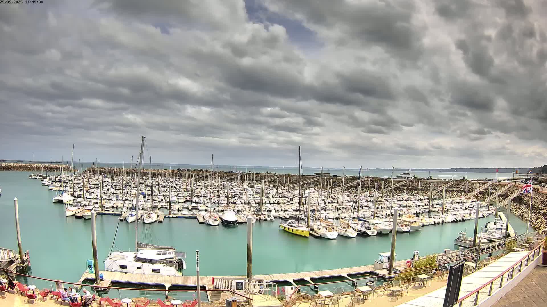 A marina filled with numerous boats is situated on calm, teal water under a cloudy sky.