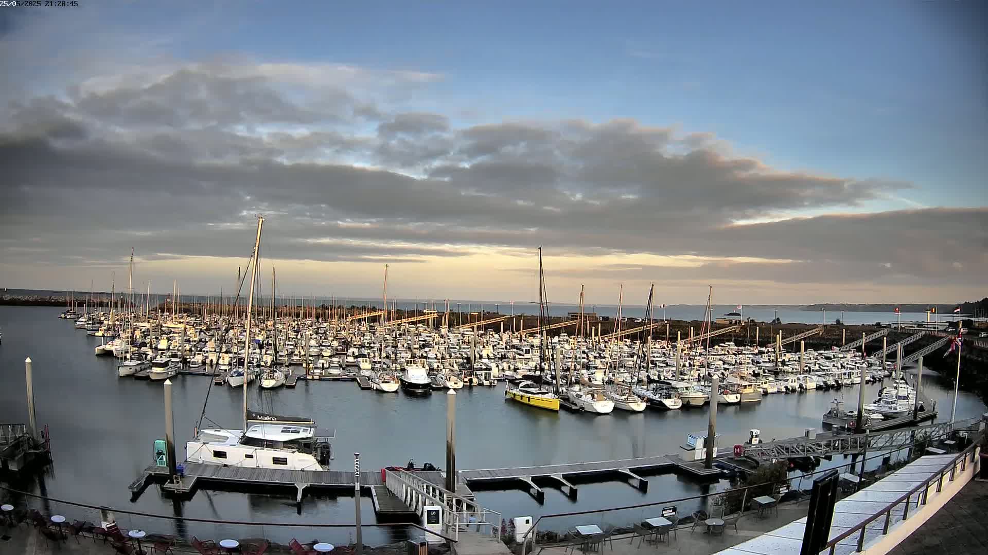 A large marina filled with numerous sailboats and motorboats under a partly cloudy sky.
