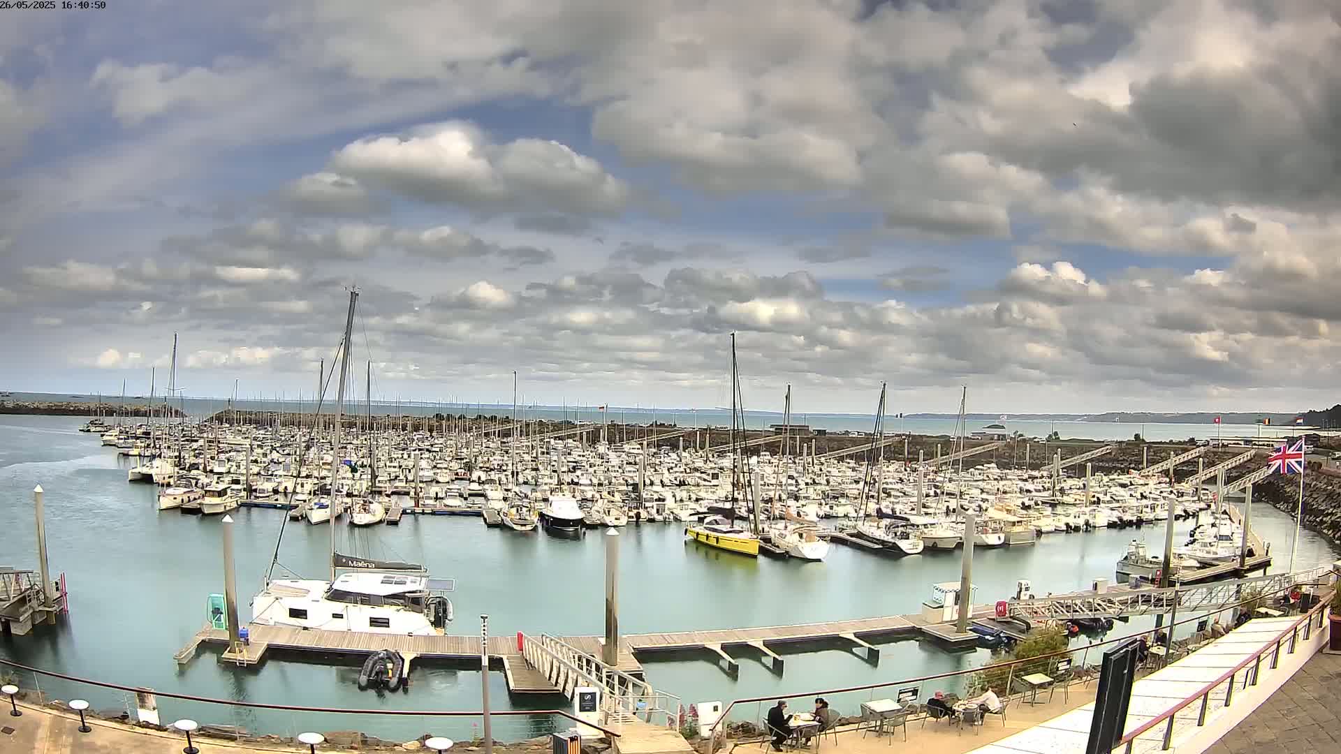 A marina filled with numerous boats of varying sizes is seen under a partly cloudy sky.