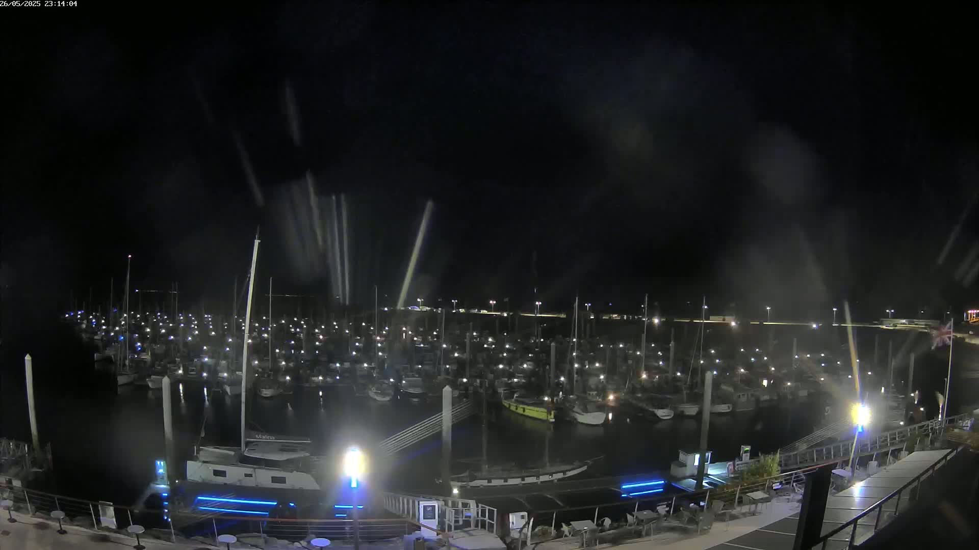 A nighttime view of a marina filled with numerous boats, under a dark sky with light rain or spray.