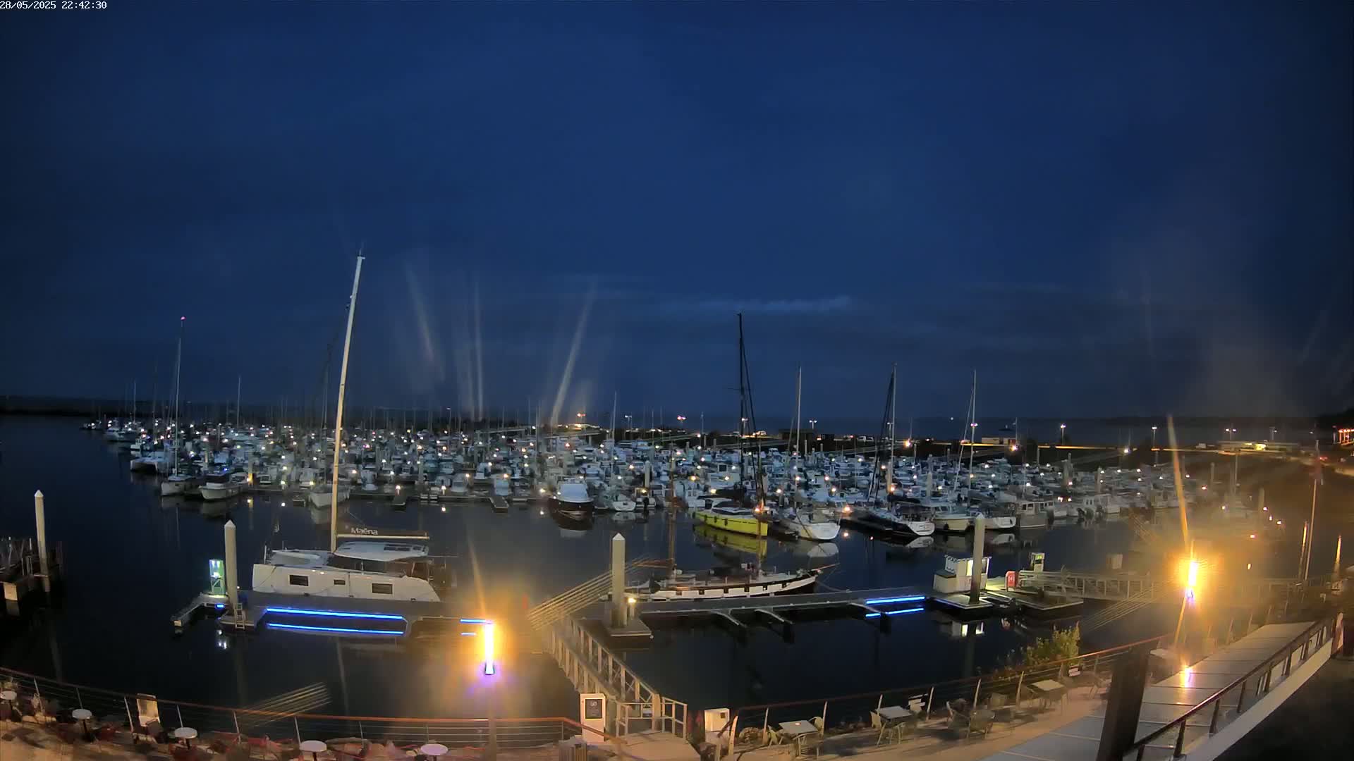 A large marina filled with numerous boats is seen at night under a dark blue, mostly clear sky.