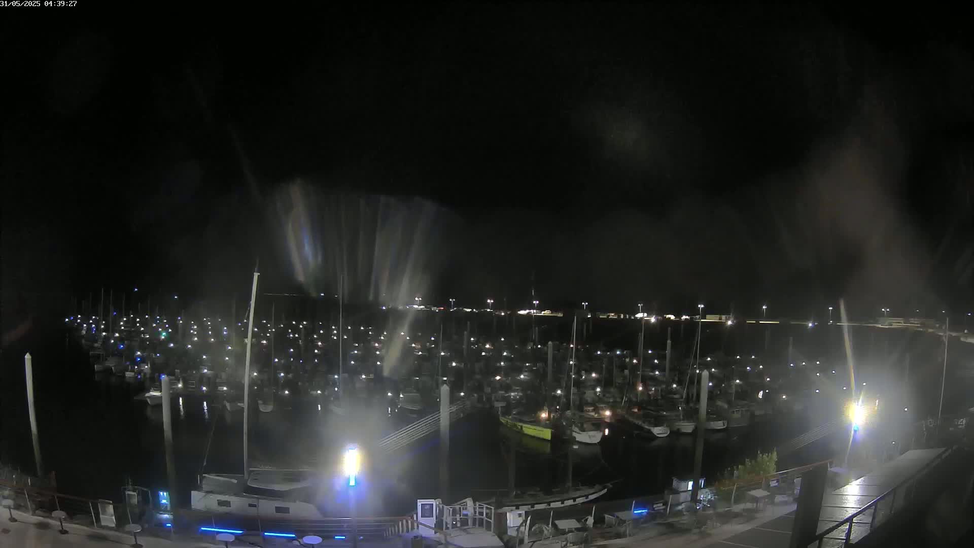 A nighttime view of a marina filled with many boats, under a dark and possibly rainy sky.