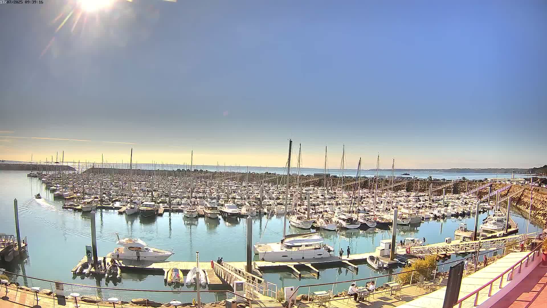 A sunny day shows a crowded marina filled with many sailboats and motorboats, with calm water and a clear sky.