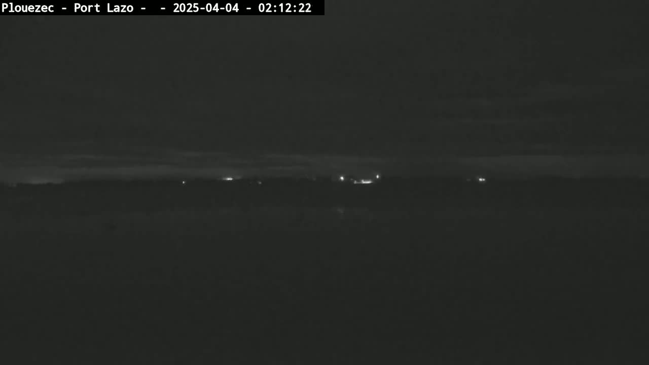 A dark, nighttime landscape shows a distant line of faint lights under a mostly clear sky.