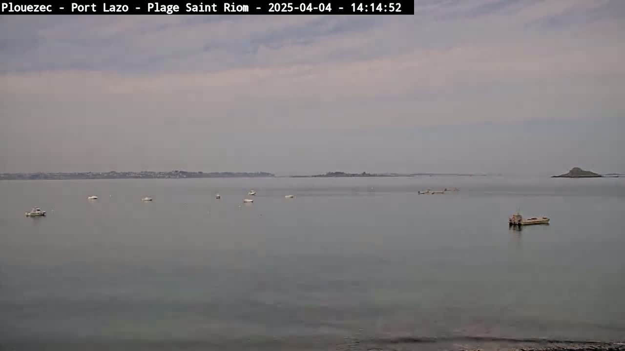 A calm, overcast day reveals a wide body of water with several small boats and a larger vessel, and land visible in the distance.