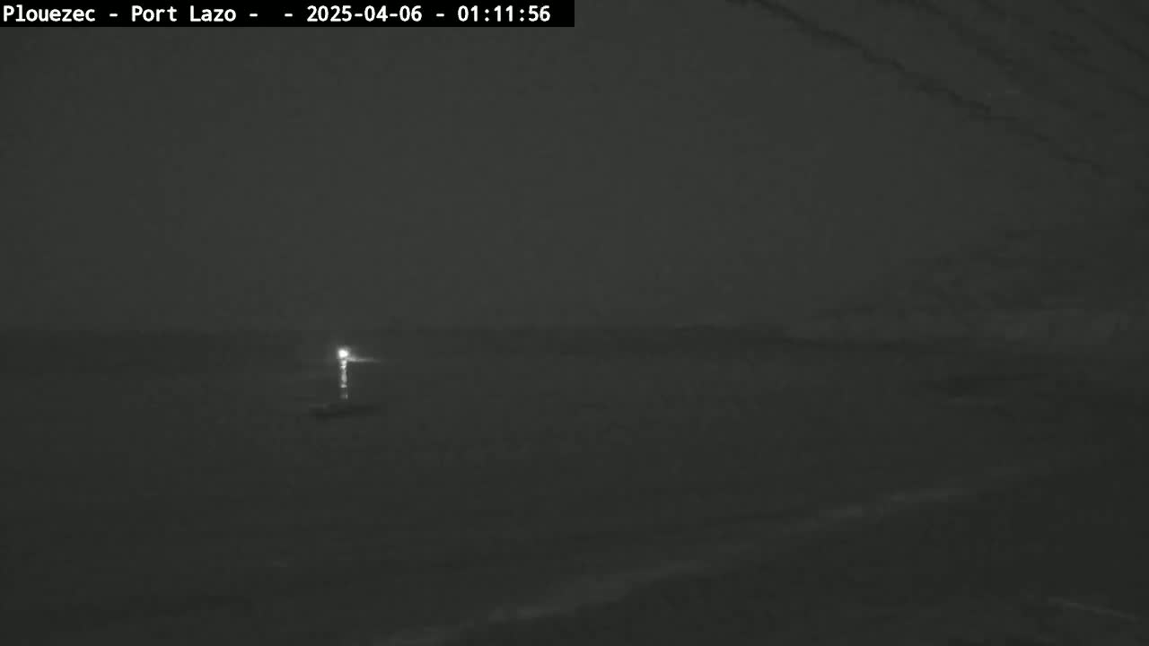 A dimly lit, nighttime scene shows a dark body of water with a faint light source in the distance.