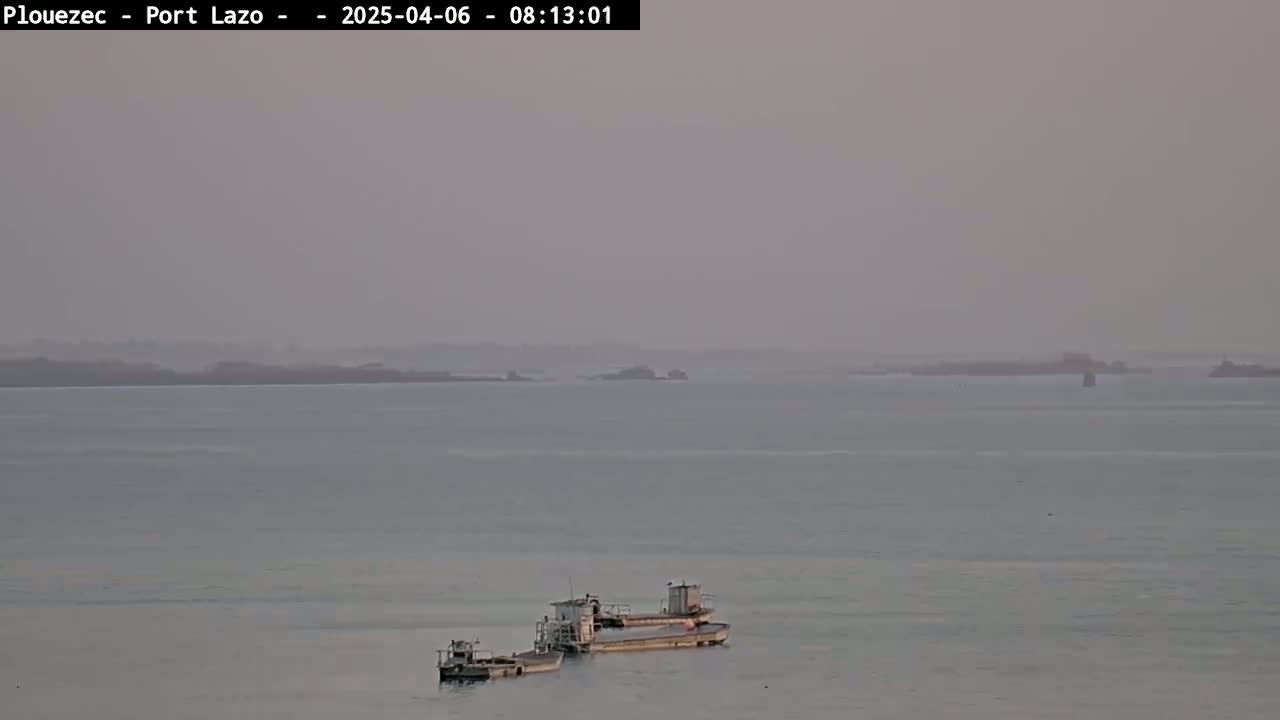 Two barges are moored in calm, hazy water near a distant shoreline.