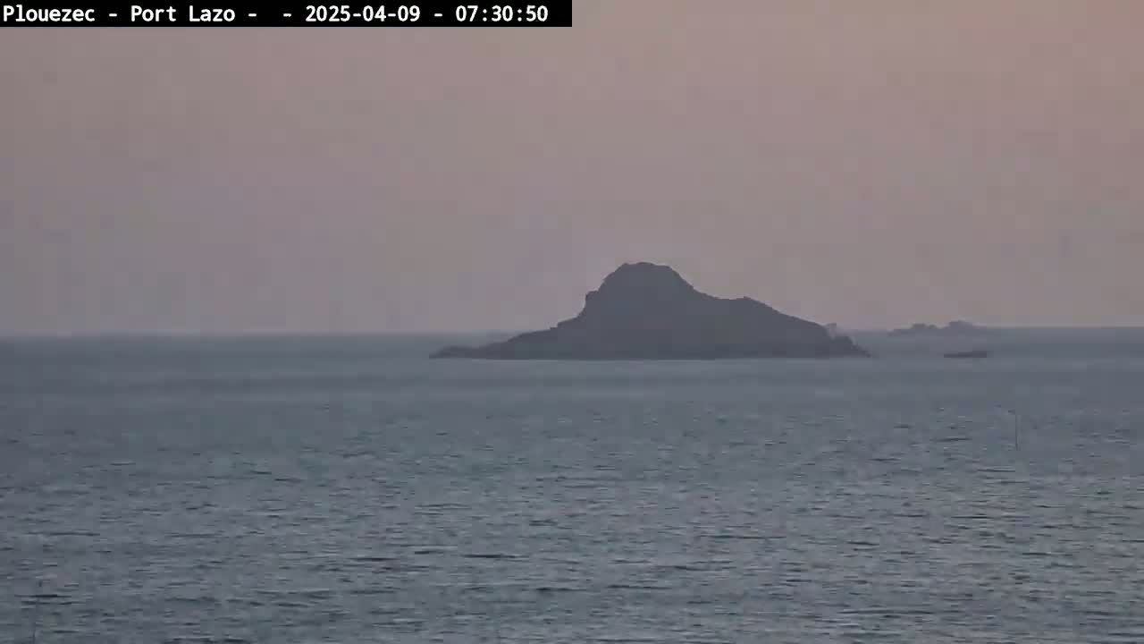 A dark island sits in a calm, hazy ocean under a dusky sky.