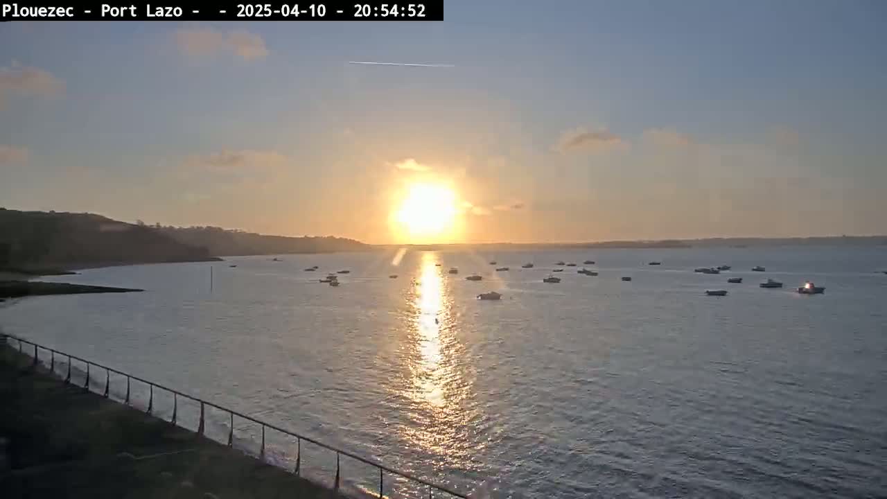 A calm body of water dotted with numerous small boats at sunset, under a mostly clear sky.
