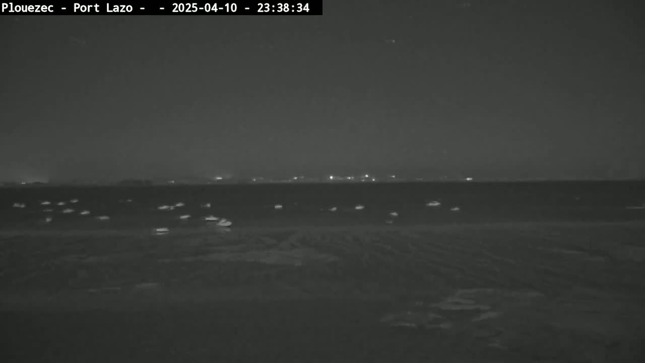 A dark, nighttime scene shows a body of water with several small lights scattered across its surface, and a distant shoreline with faint lights visible.