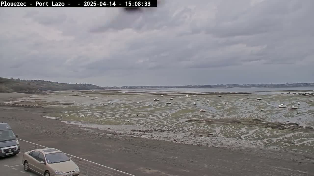 A wide shot shows a beach with numerous small boats resting on exposed mudflats under an overcast sky.