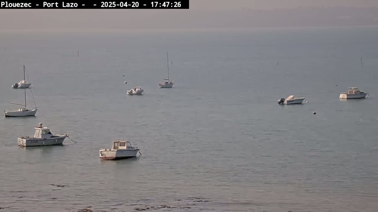 Several small boats and sailboats are moored in calm, hazy waters.