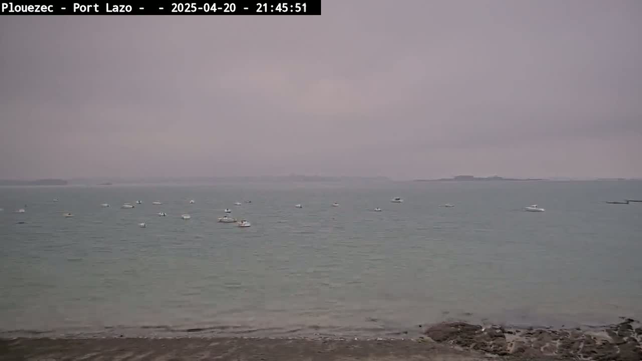 Several small boats are scattered across a calm body of water under an overcast sky.