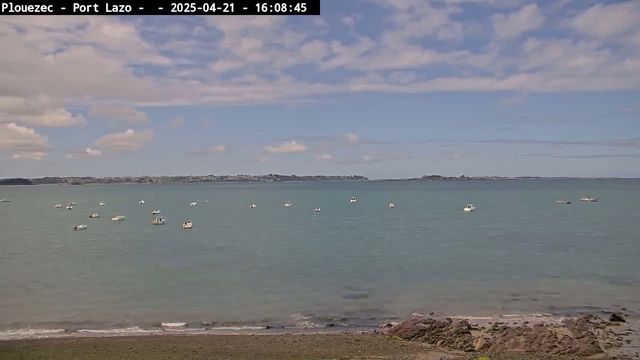 A calm body of water with several small boats and a distant shoreline under a partly cloudy sky.