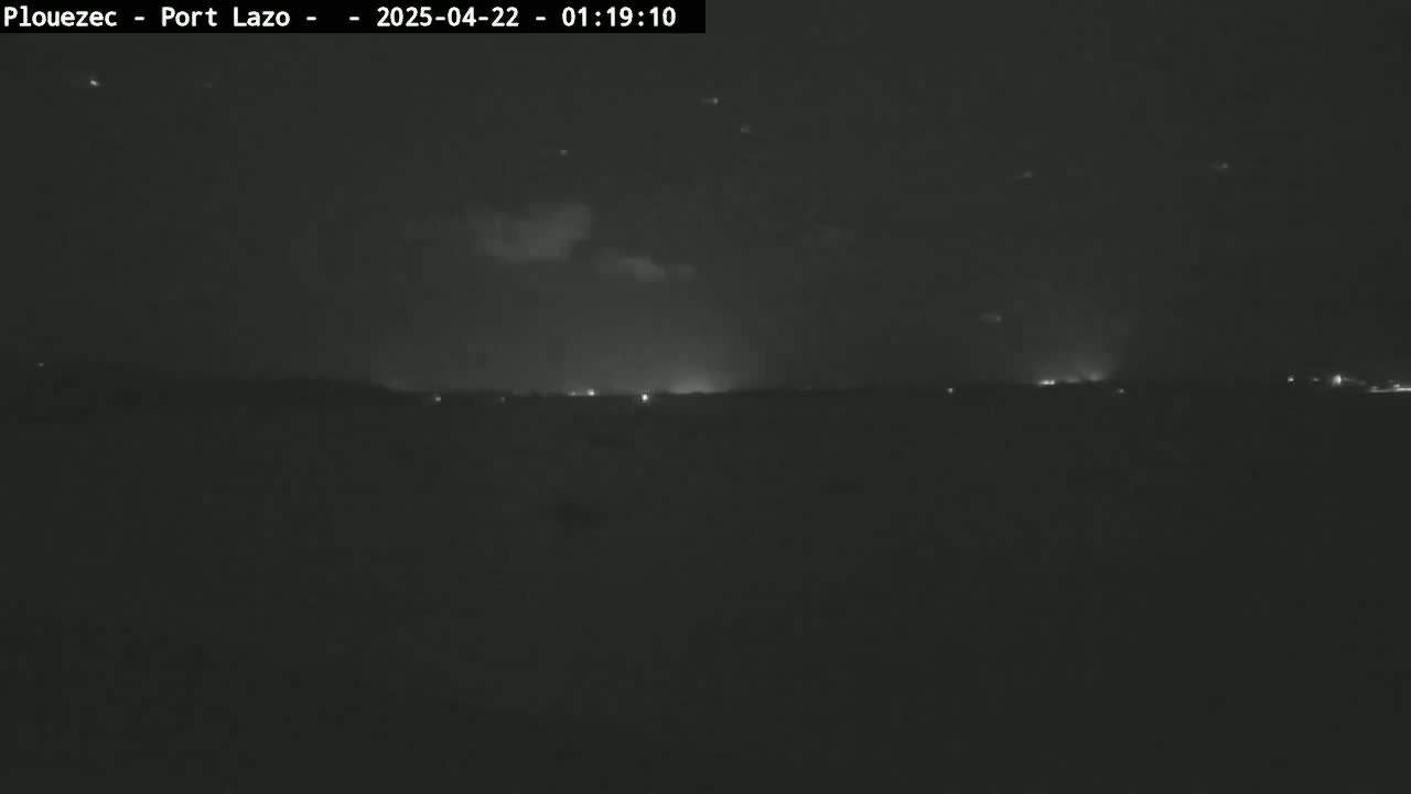 A nighttime, low-light view of a flat landscape with a few distant lights under a dark sky.