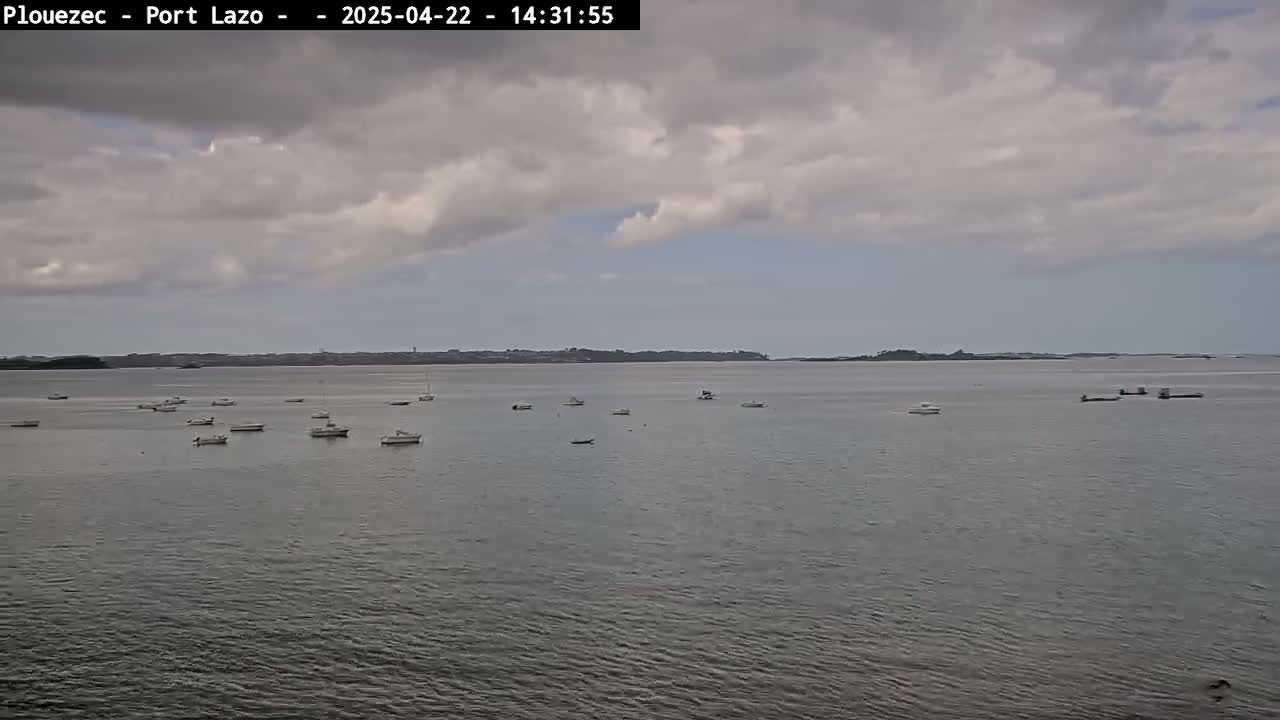 Several small boats are scattered across a calm body of water under a cloudy sky.