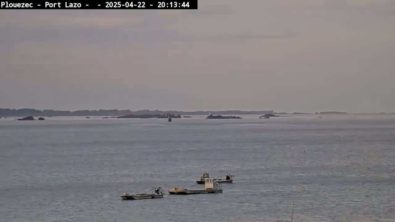 Three small boats are visible on a calm, gray body of water with a distant, low-lying landmass under an overcast sky.