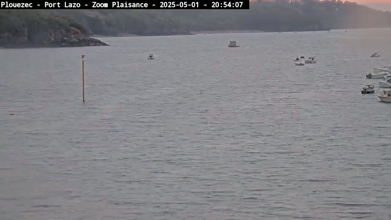 Several small boats are scattered across a calm body of water near a shoreline under a twilight sky.
