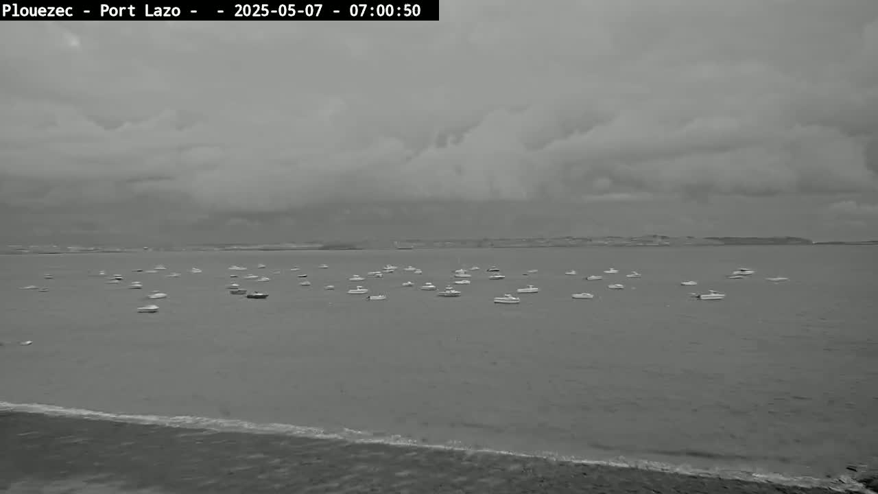 Numerous small boats are at anchor in a calm body of water under a cloudy sky.