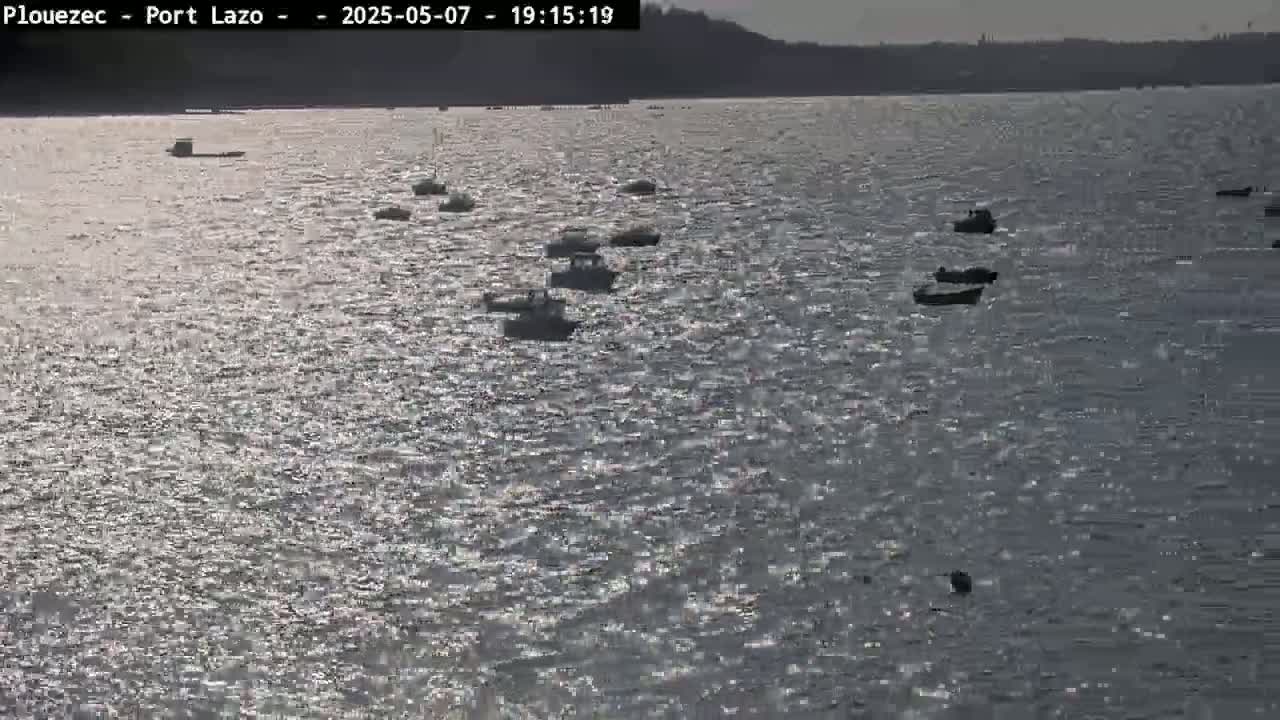 Several small boats are scattered across a body of water under a mostly sunny sky with a slight ripple on the water's surface.