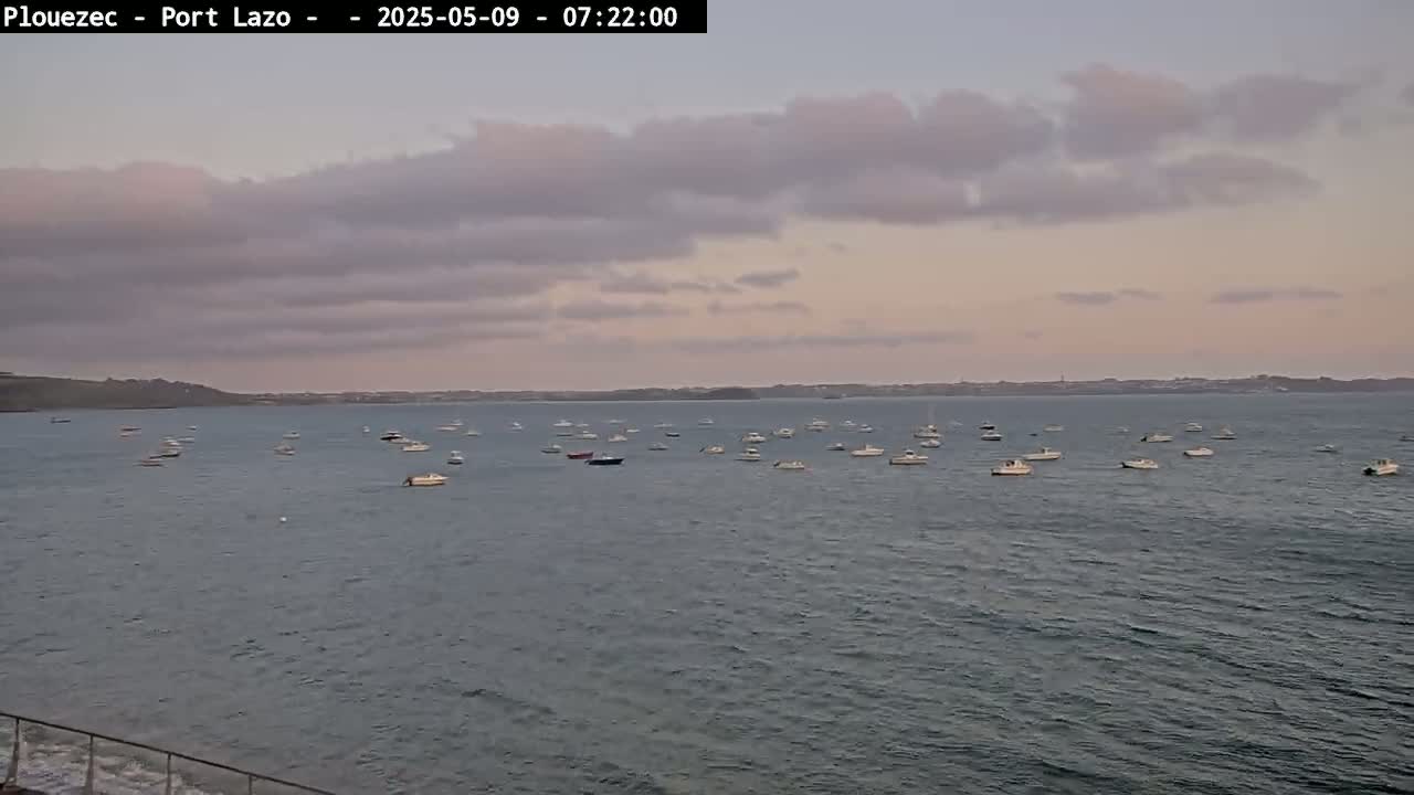 Numerous small boats are moored in a calm body of water under a partly cloudy, dusky sky.