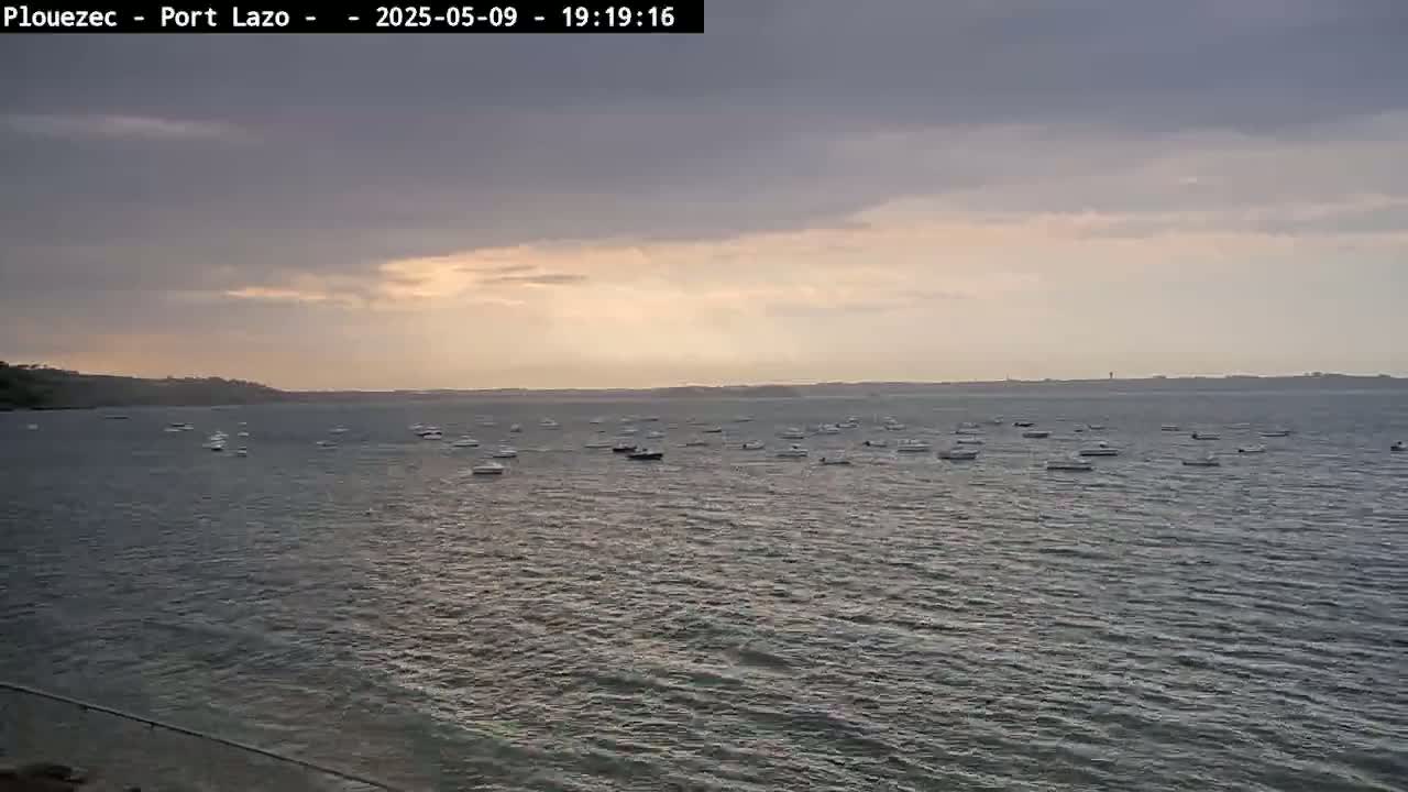 Numerous small boats are scattered across a calm body of water under a cloudy, sunset sky.