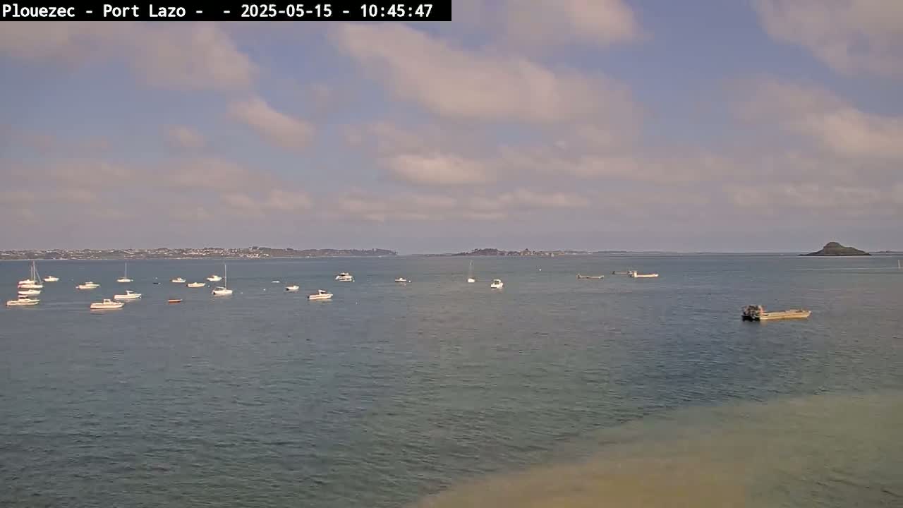 Several small boats are anchored in a calm body of water under a partly cloudy sky.