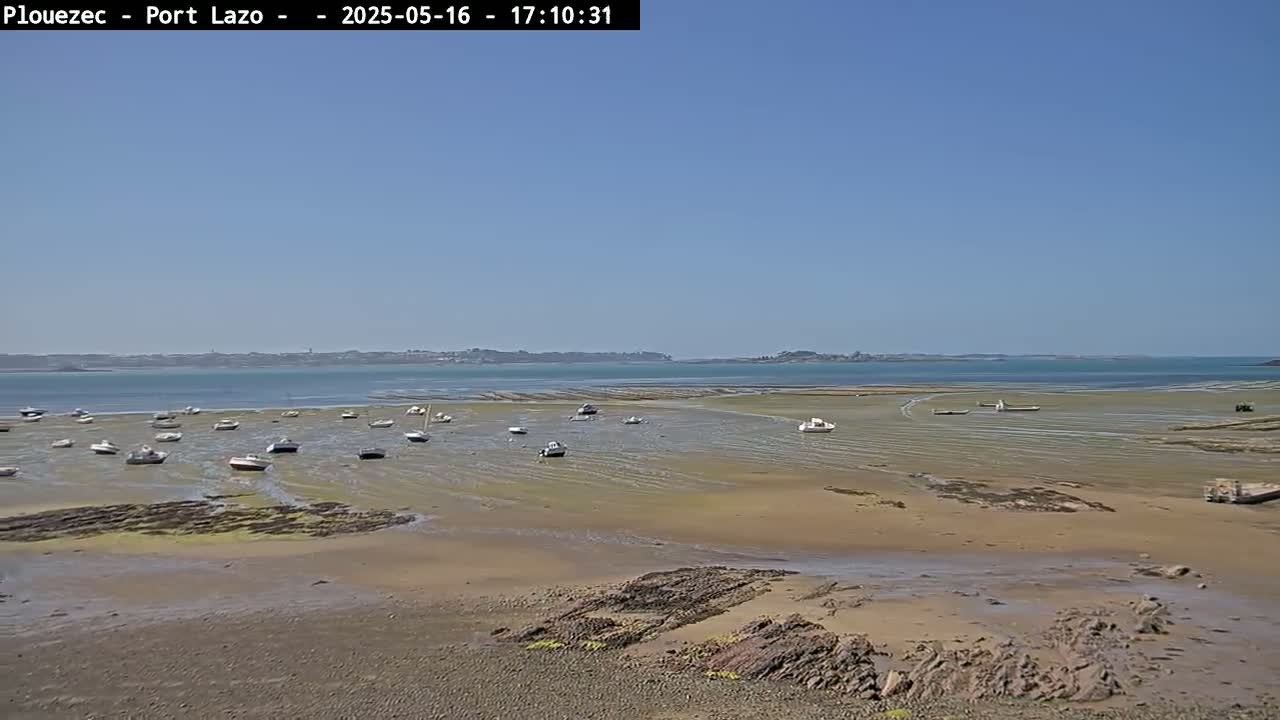 A wide sandy expanse reveals numerous small boats grounded at low tide under a clear blue sky.