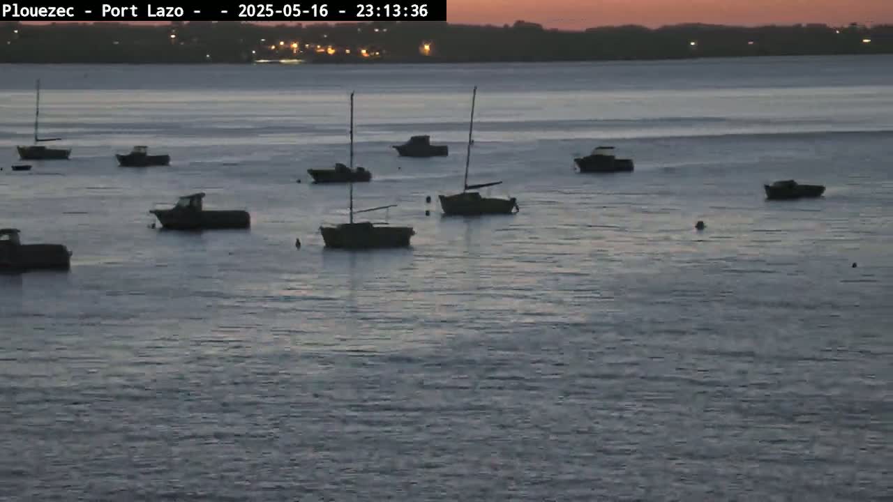 Several small boats are moored in calm water at dusk, under a pinkish-orange sky.