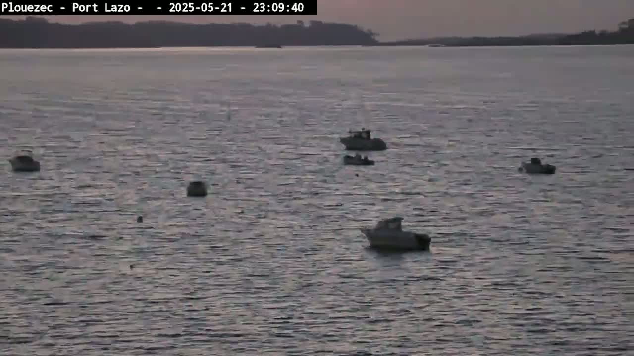 Several small boats are moored in calm water at dusk, with a dark landmass visible in the distance.