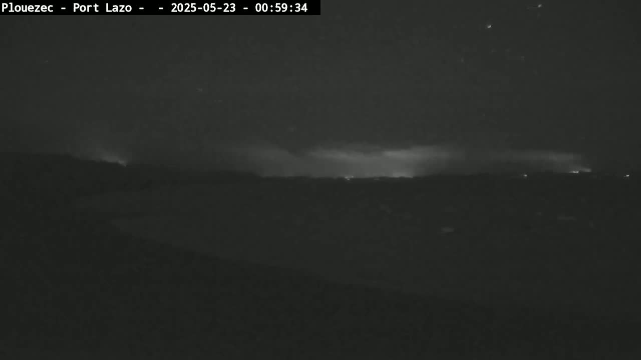 A nighttime, low-light view shows a dark landscape with faint lightning in the distance under a cloudy sky.
