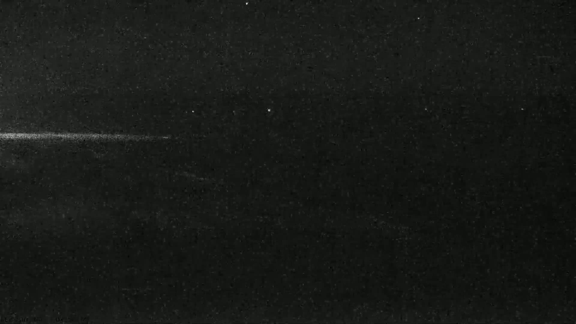A nighttime image shows a faint horizontal line of light against a dark, grainy background.