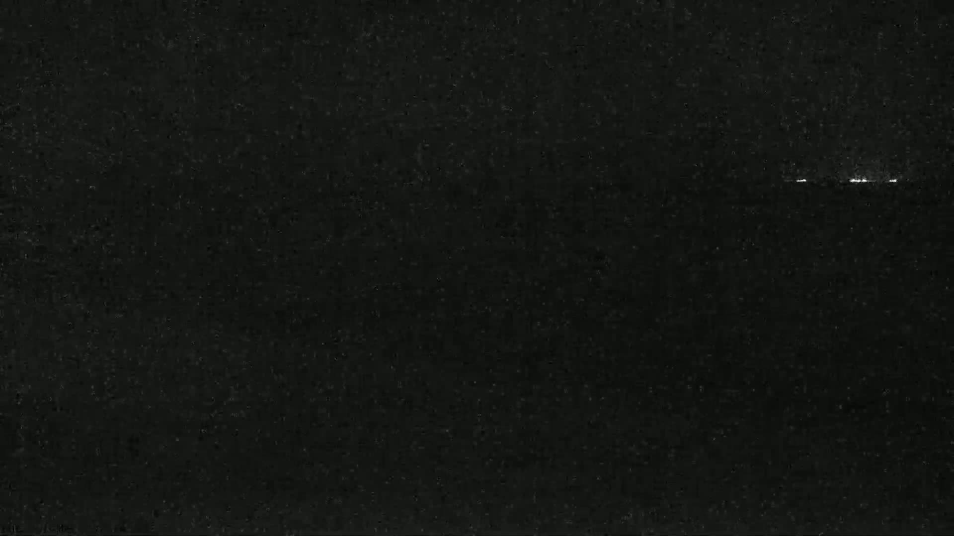 A dark, grainy image shows a faint line of lights on the horizon at night.