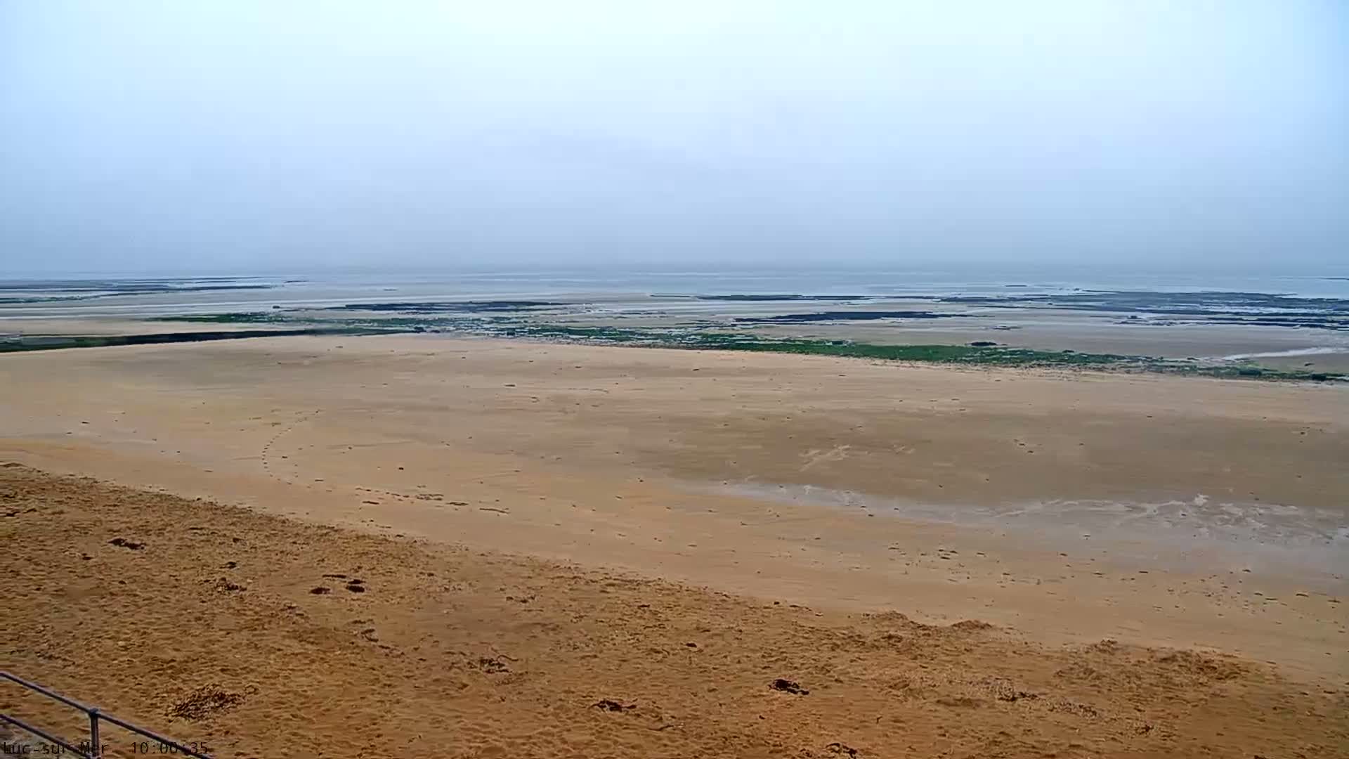 A wide expanse of sandy beach slopes down to a calm, grey sea under an overcast sky.