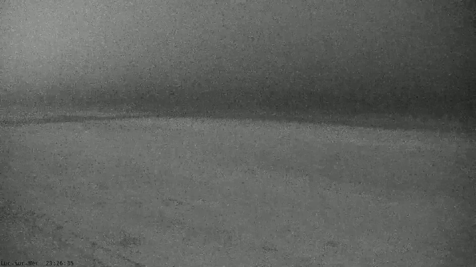 A blurry, dark gray image shows a flat, indistinct horizon line under an overcast sky.