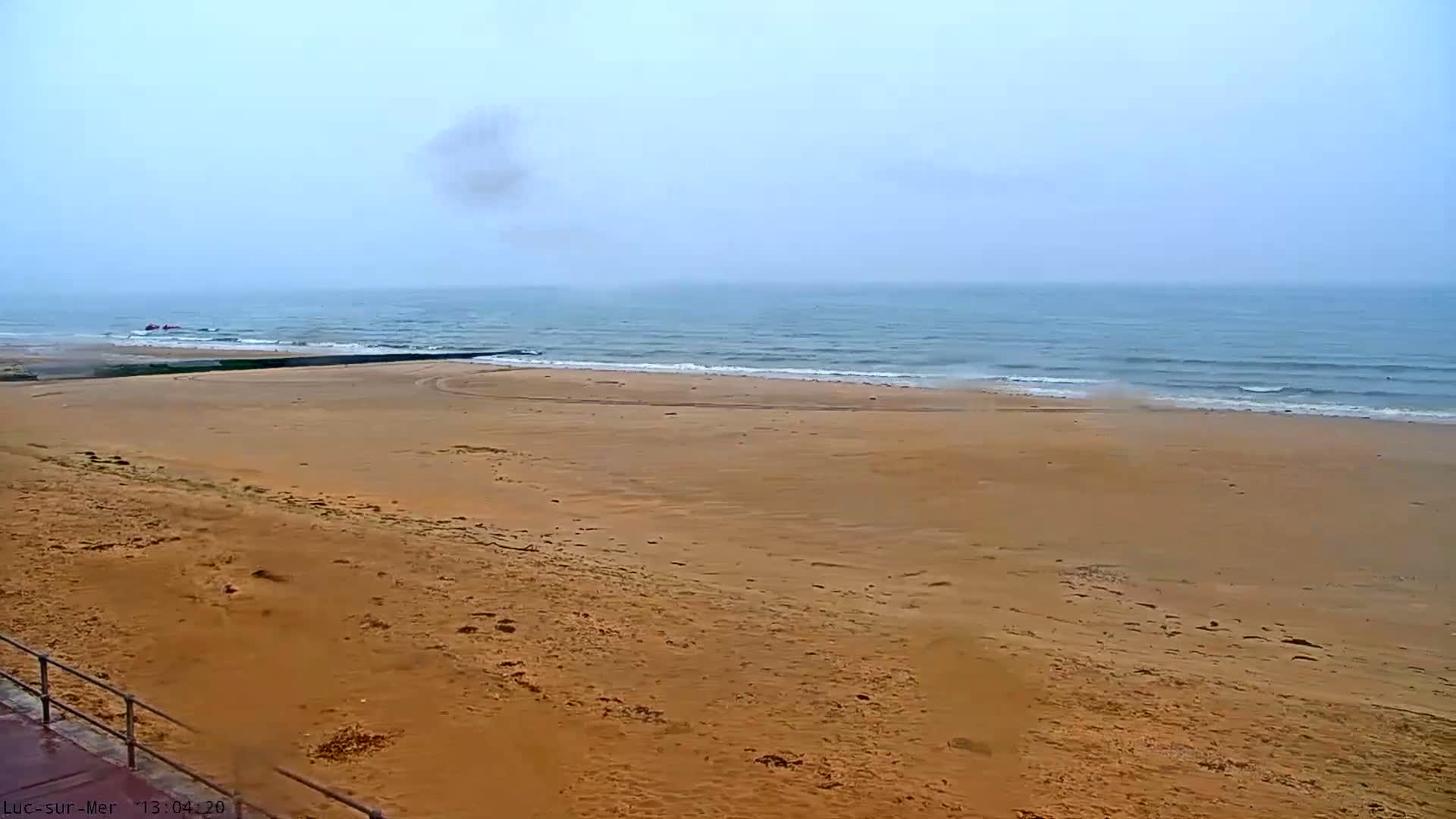 A wide sandy beach stretches to a calm, somewhat hazy ocean under a mostly clear sky.