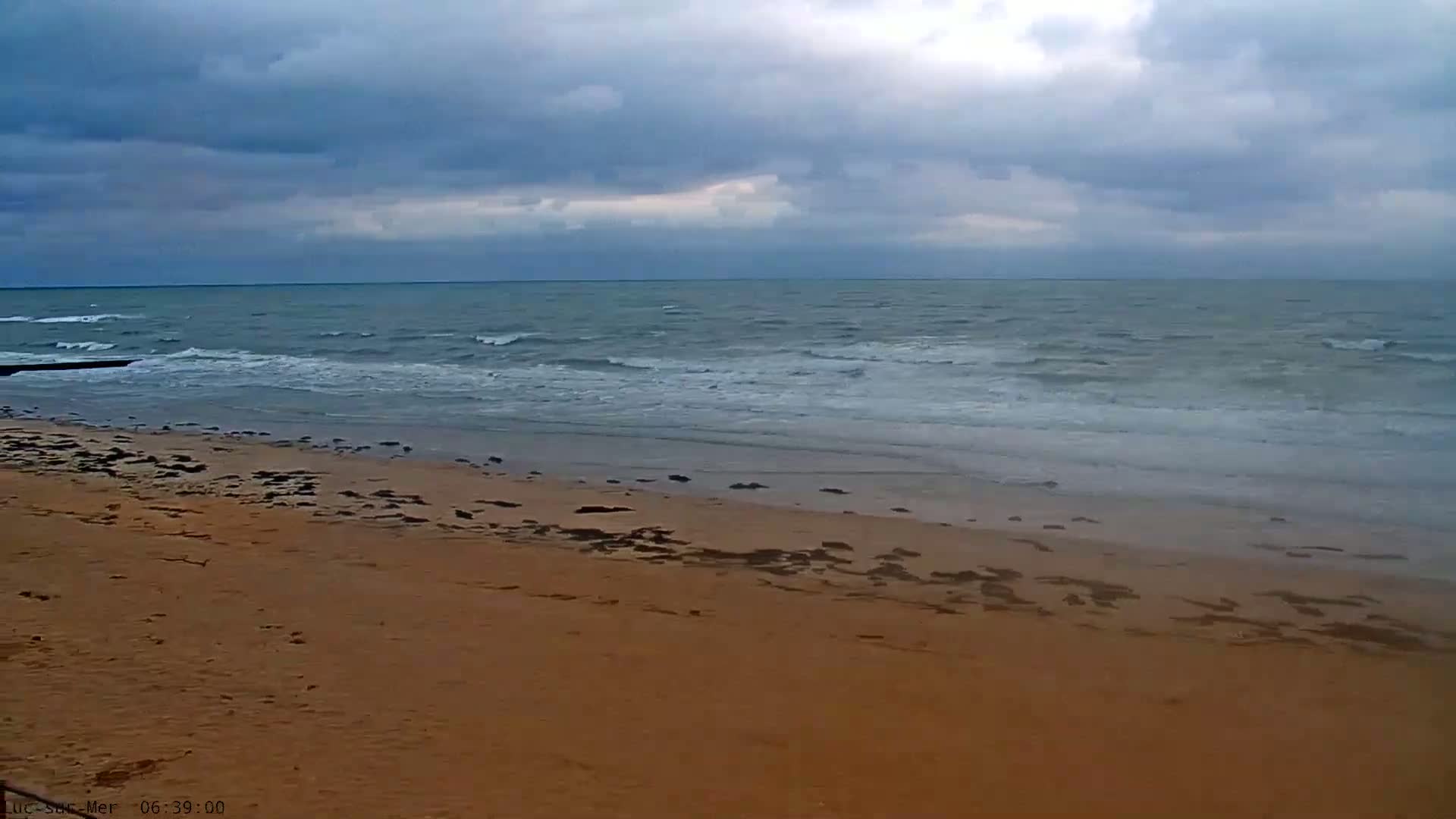 A sandy beach stretches to a grey, overcast sky and a wavy ocean.