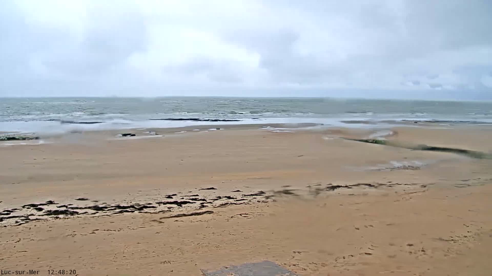 A wide sandy beach stretches to a choppy sea under an overcast sky.