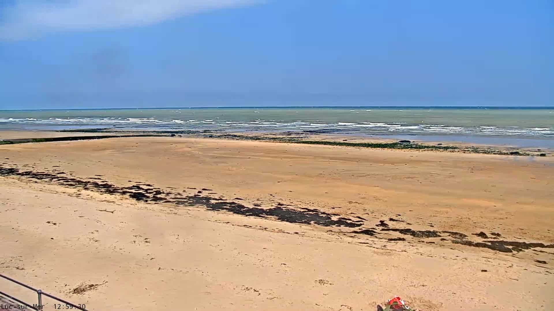 A sandy beach stretches towards a calm sea under a clear blue sky.