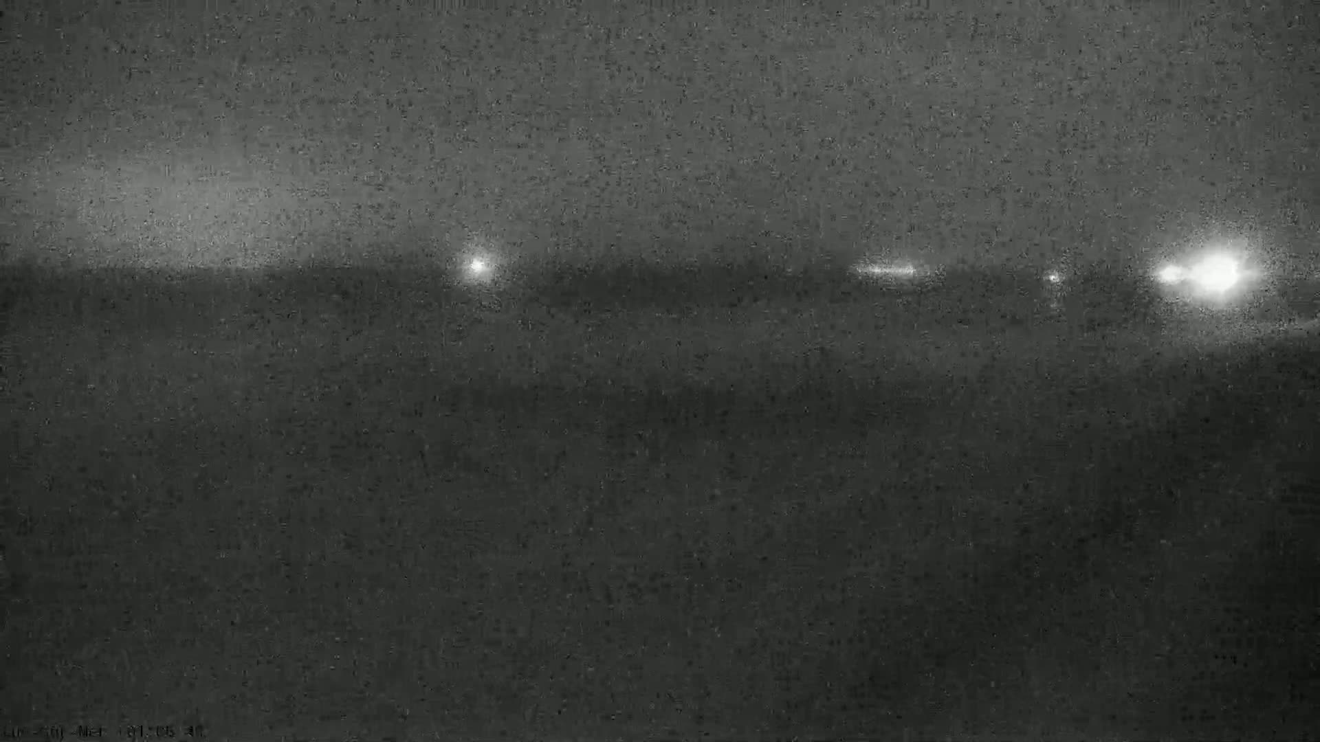 A nighttime, low-visibility view of a flat landscape with distant lights.