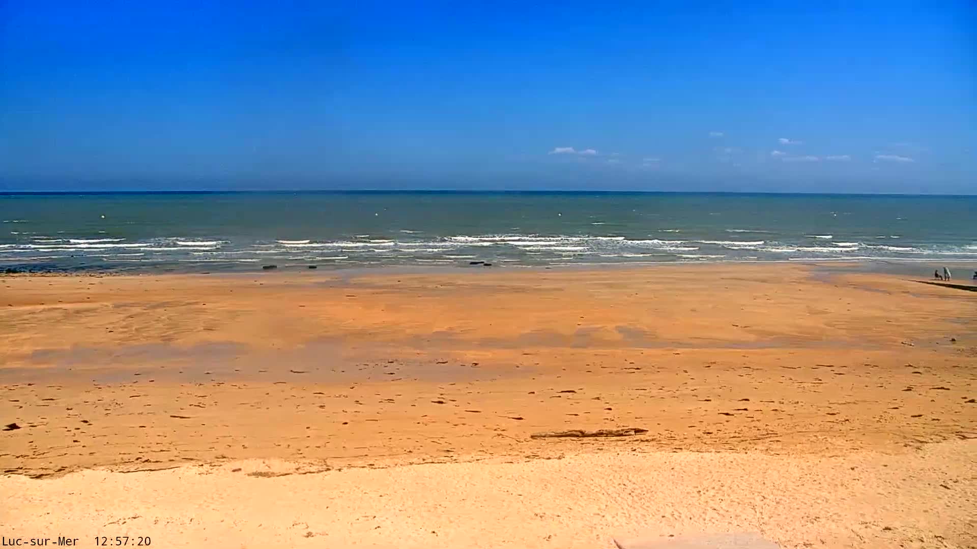 A wide sandy beach stretches to a calm sea under a clear blue sky.